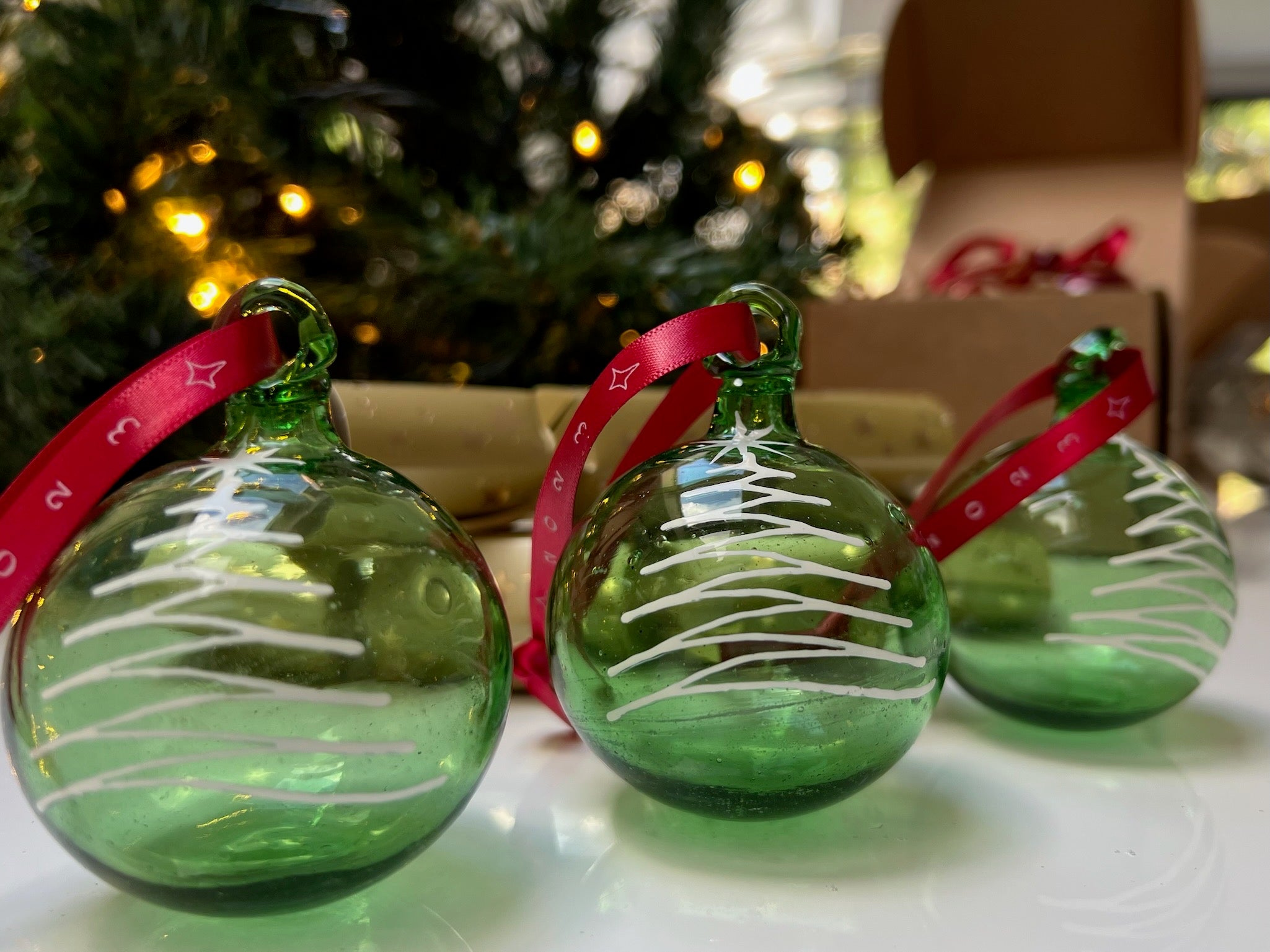 Green glass Christmas ornament painted with white tree on red ribbon